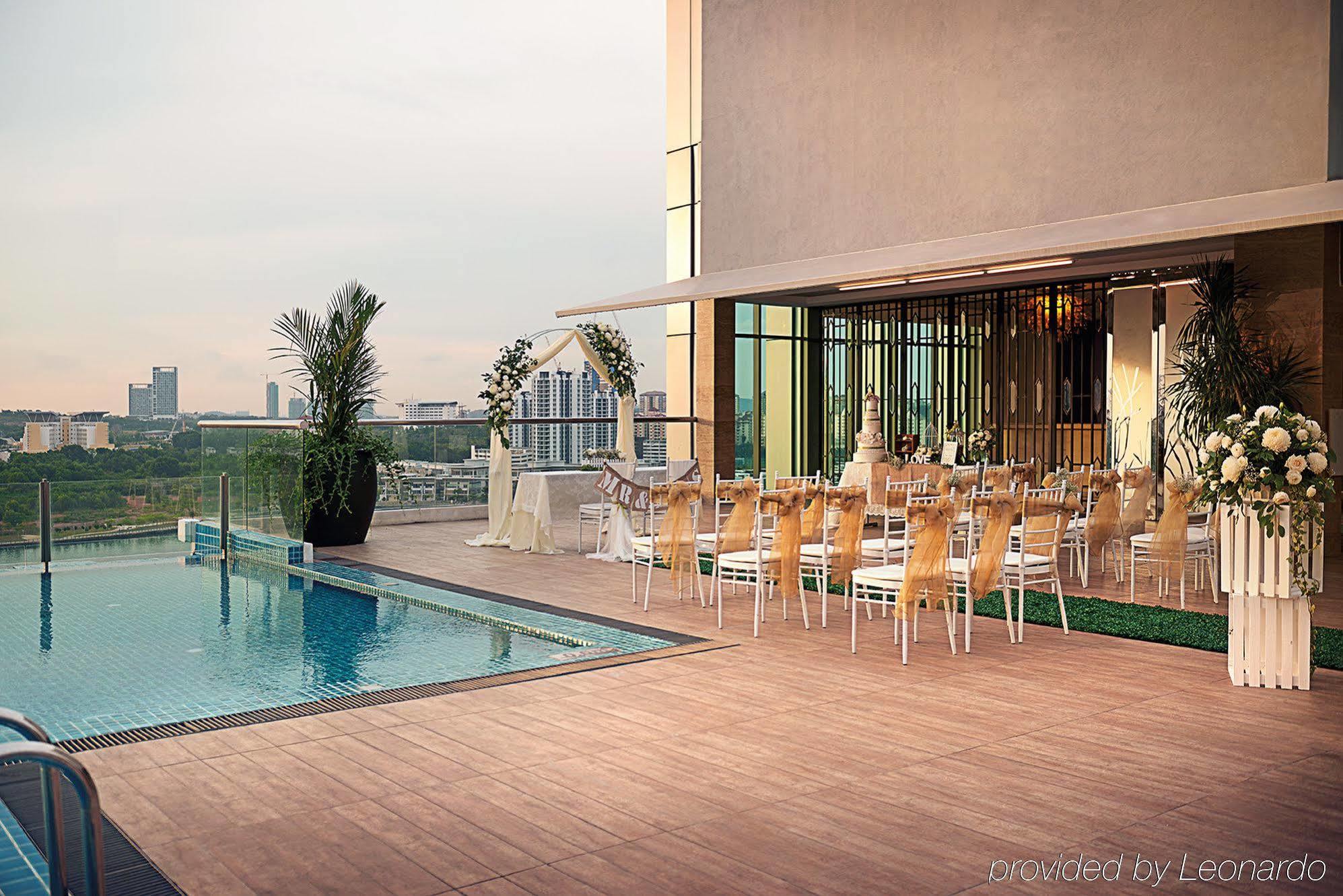 Отель Dorsett Путраджая Экстерьер фото The photo shows an outdoor area featuring a swimming pool adjacent to a spacious terrace. On the terrace, there are several elegantly arranged tables and chairs, suggesting it is set up for an event, possibly a wedding or a formal gathering. The back