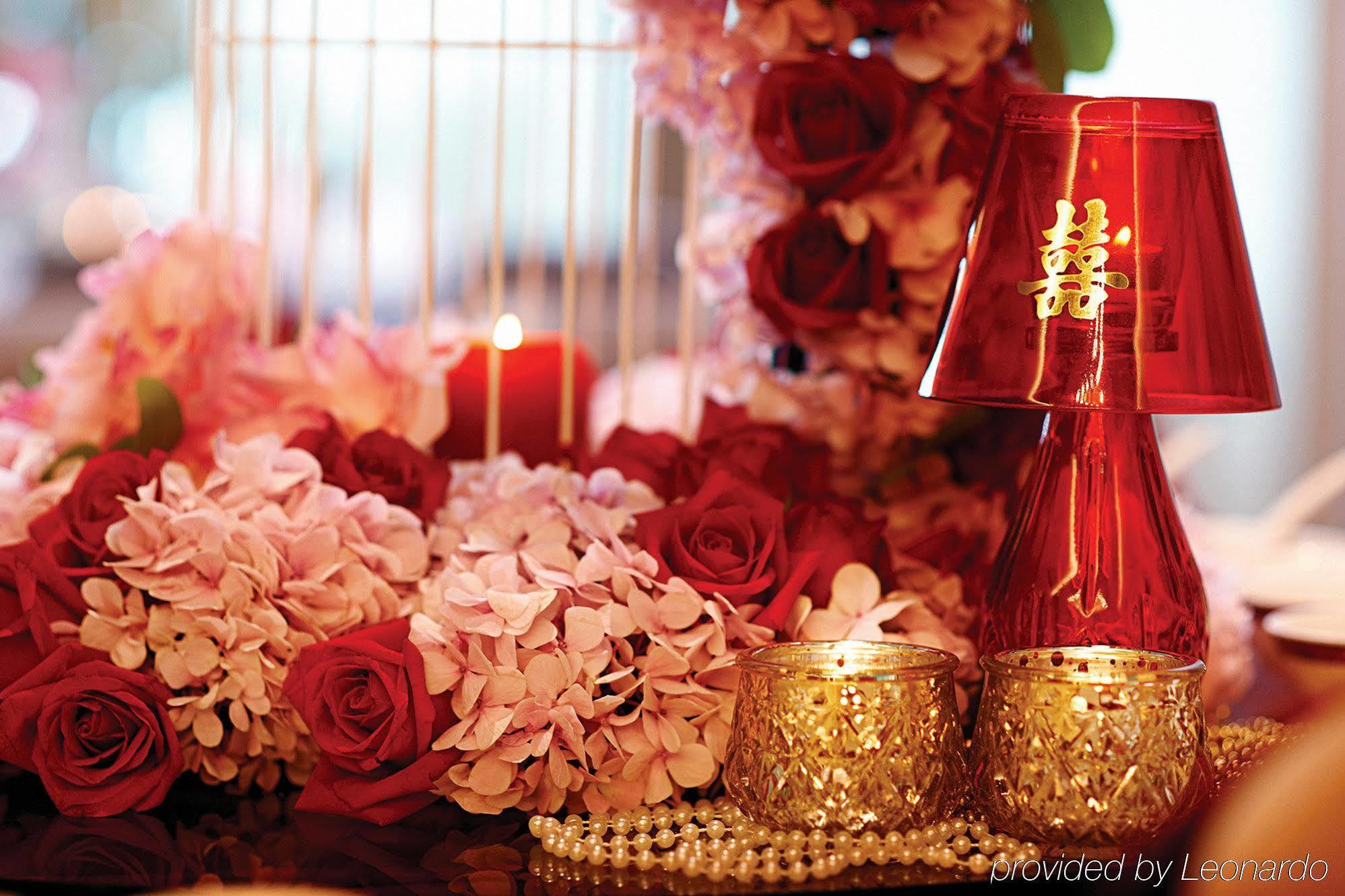 Отель Dorsett Путраджая Экстерьер фото The photo features a beautiful arrangement that includes a mix of floral elements such as pink and red roses, along with other delicate flowers. In the center, there are decorative items like a shiny red vase or lamp with a traditional symbol on it, 