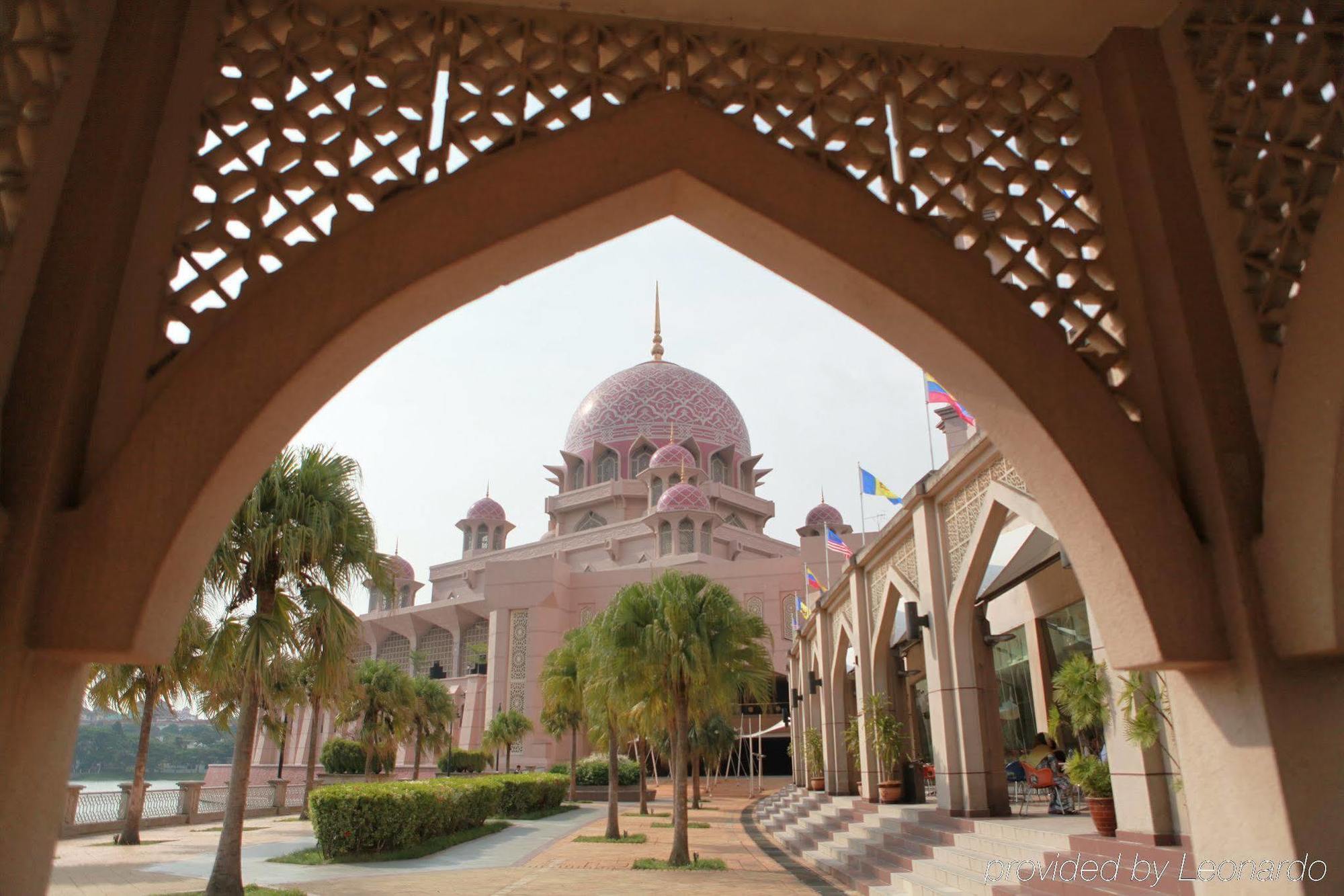 Отель Dorsett Путраджая Экстерьер фото The photo shows an impressive architectural structure, likely a mosque, characterized by its pink dome and ornate design. The building features multiple domes and minarets. In the foreground, there is a beautifully crafted archway with intricate latt