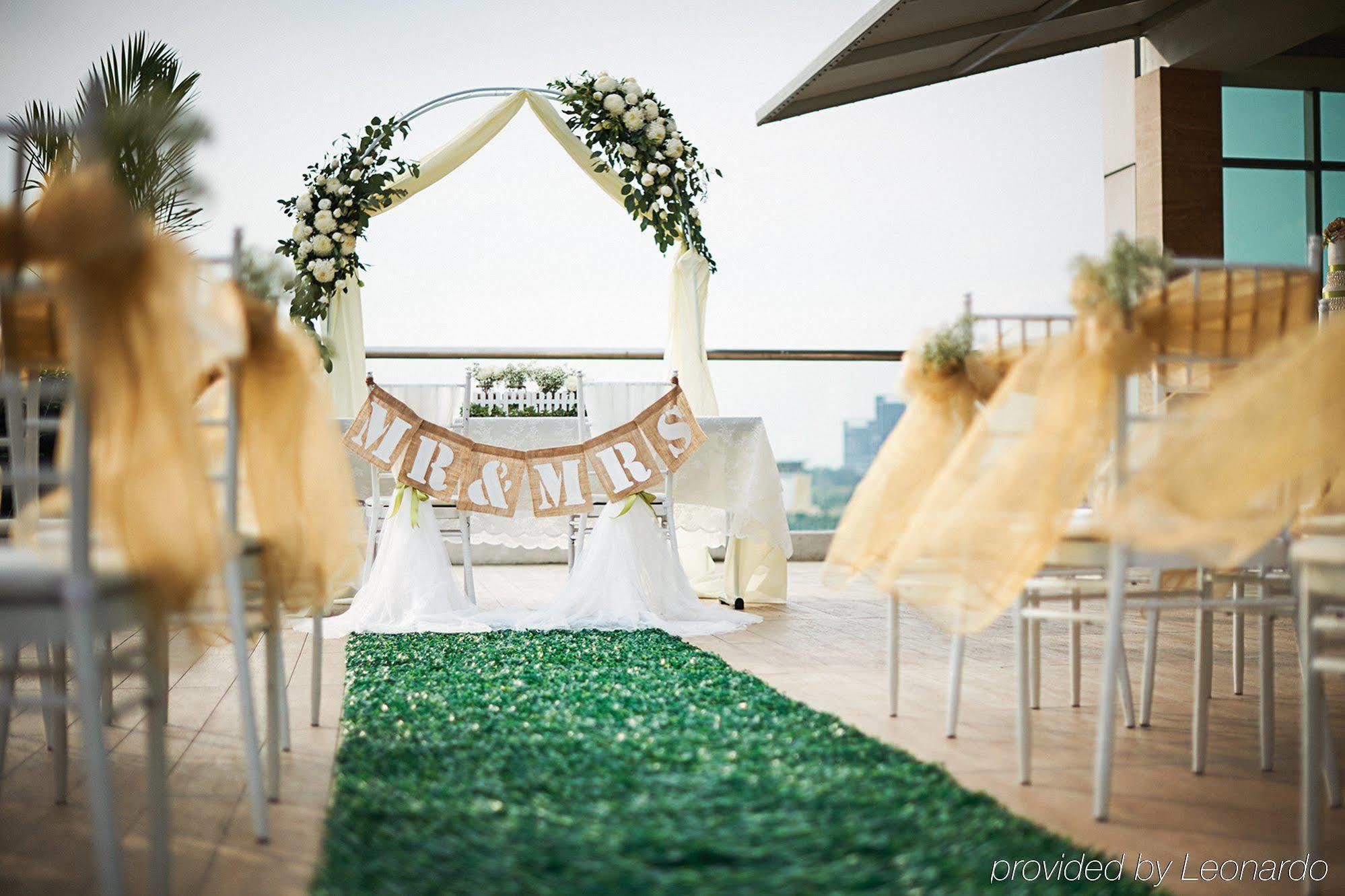 Отель Dorsett Путраджая Экстерьер фото The photo depicts a beautifully arranged outdoor wedding setting. In the foreground, there is a green carpet leading to an altar or archway adorned with flowers and draped fabric. Above the altar, a banner reads "MR & MRS," indicating it is a wedding