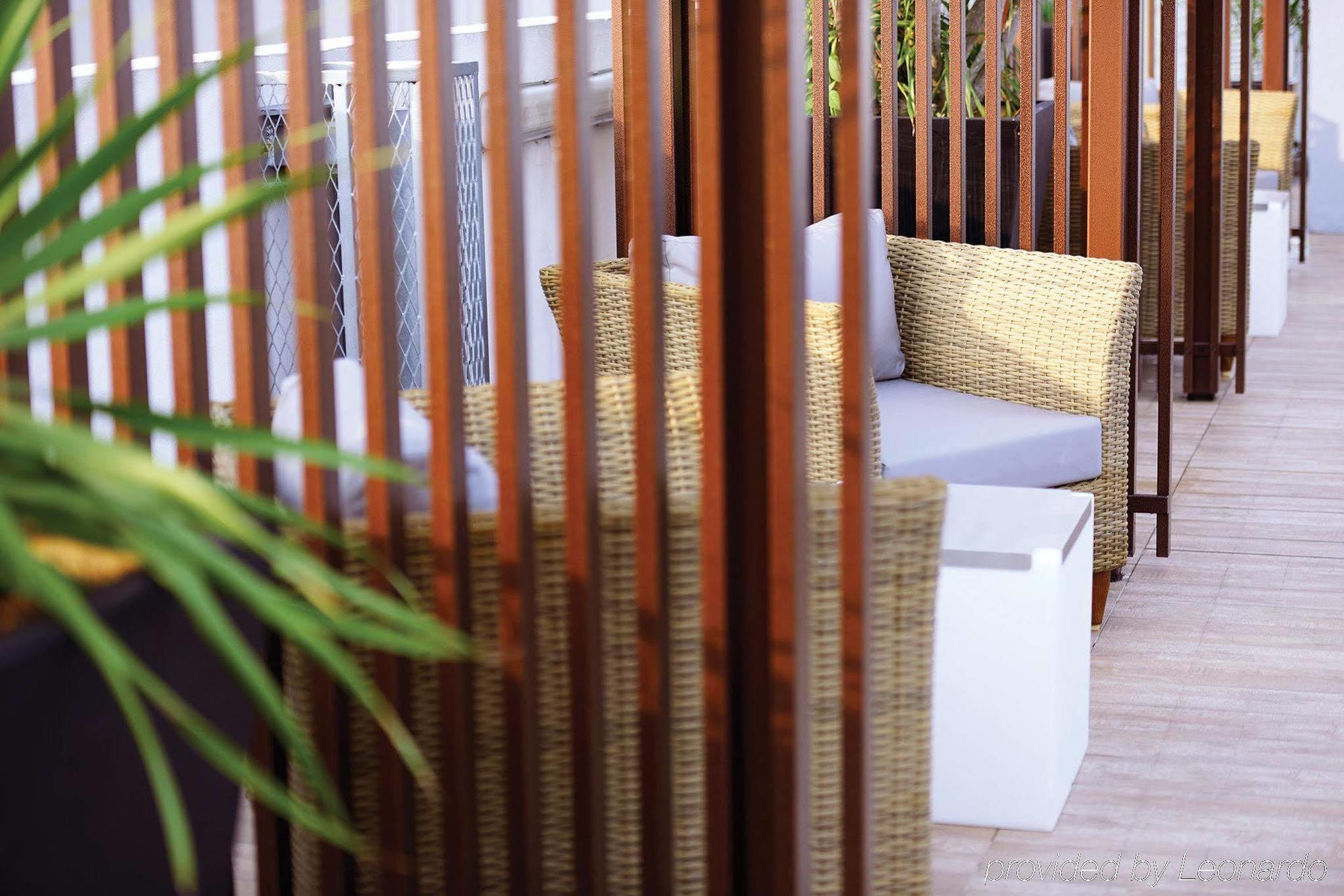 Отель Dorsett Путраджая Экстерьер фото The photo shows a cozy outdoor seating area. There are two wicker chairs with gray cushions positioned near a small white table. The seating is partially surrounded by wooden slats, which create a sense of privacy and separation from the rest of the 